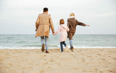 Back view of a young family with a little daughter having fun at the beach together and running