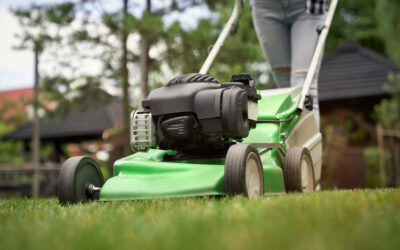 Close up of female legs of gardener using green lawn mower on backyard. Selective focus of woman working in summer, cutting grass in backyard. Concept of gardening, work, nature.